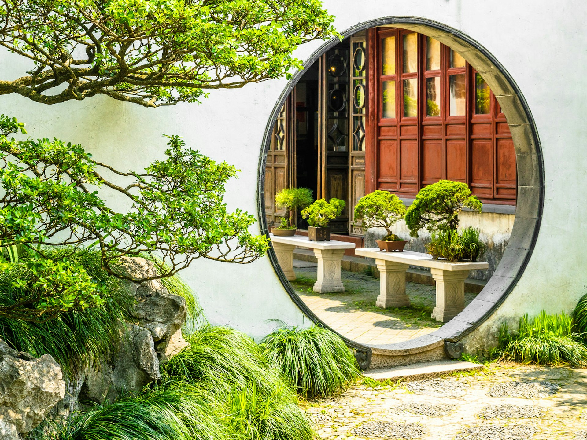 A round moon gate surrounded by white walls and green trees in Suzhou's the Garden of the Master of the Nets © Zharov Pavel / Shutterstock