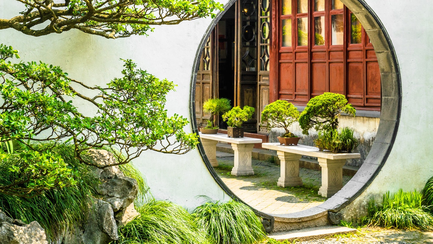 A round moon gate surrounded by white walls and green trees in Suzhou's most famous garden, the Humble Administrator's Garden © Zharov Pavel / Shutterstock