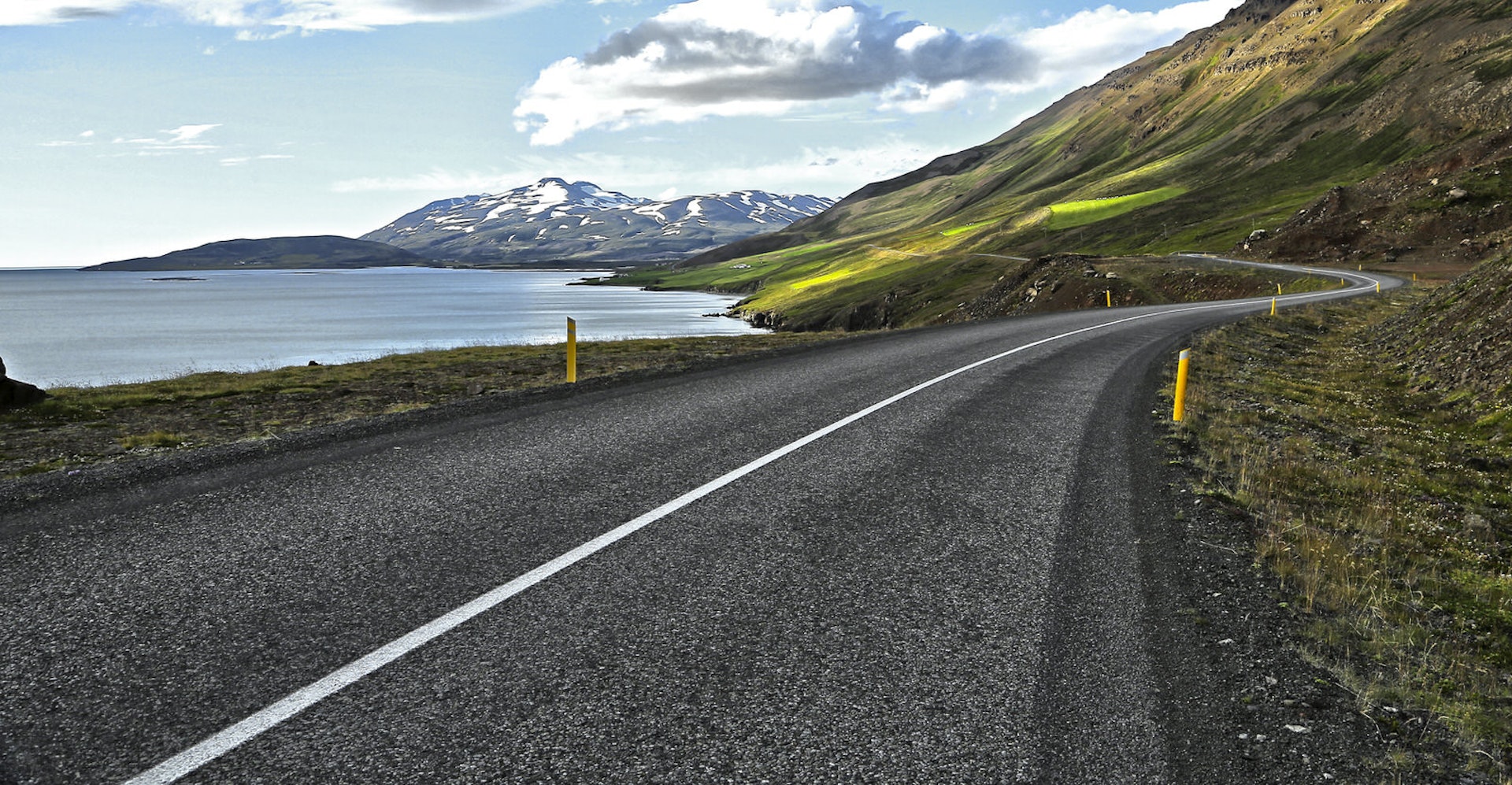 A curving road through green landscape on edge of Eyjafjordur with snow capped mountains in distance calls to those wanting to impart on a North Iceland road trip © IVANVIEITO / Getty Images