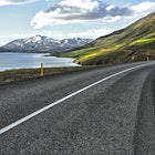 curving-road-cuts-through-green-landscape-on-edge-of-eyjafjordur-with-snow-capped-mountains-in-distance