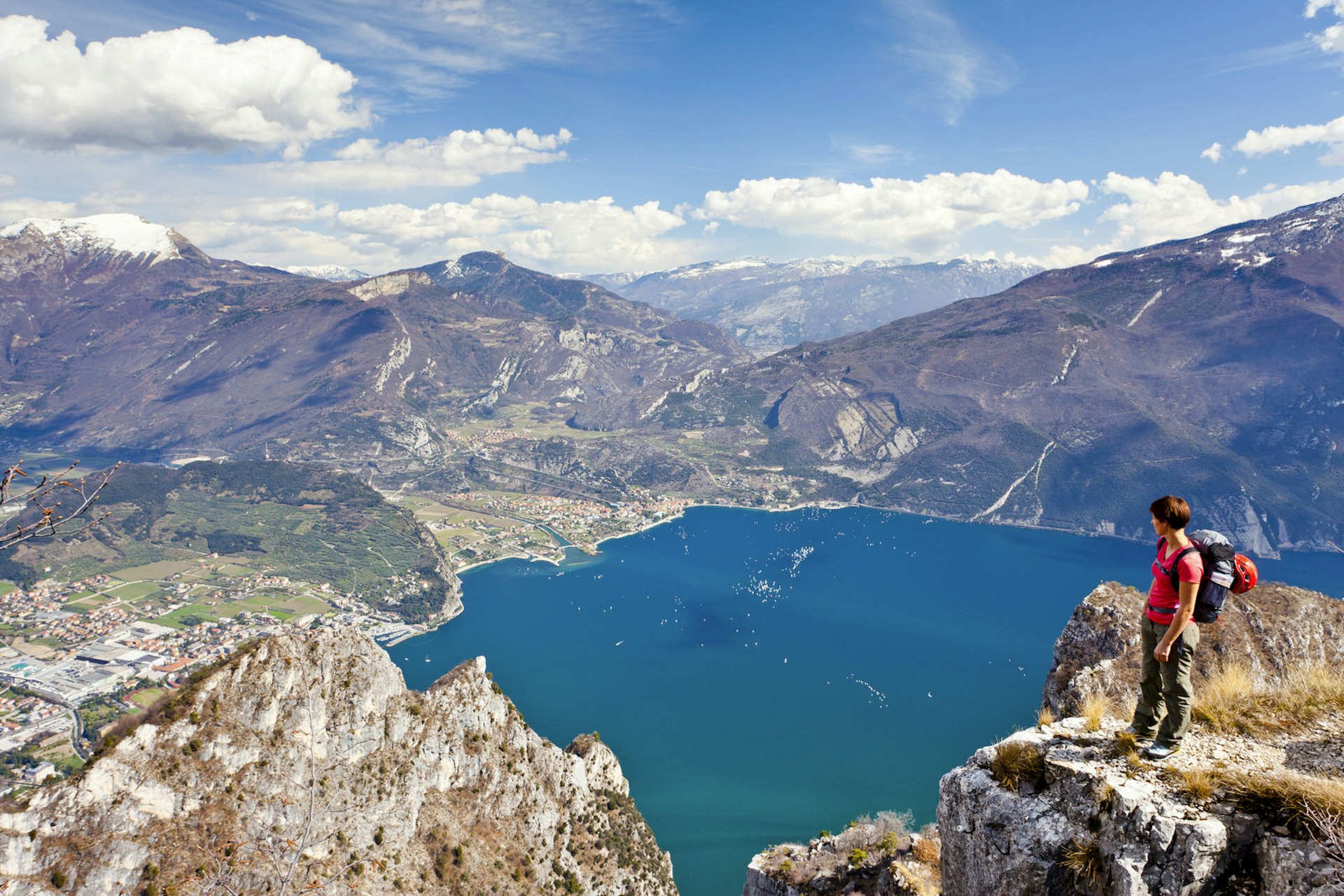 A female hiker stands atop a rock overlooking Lake Garda and distant mountains