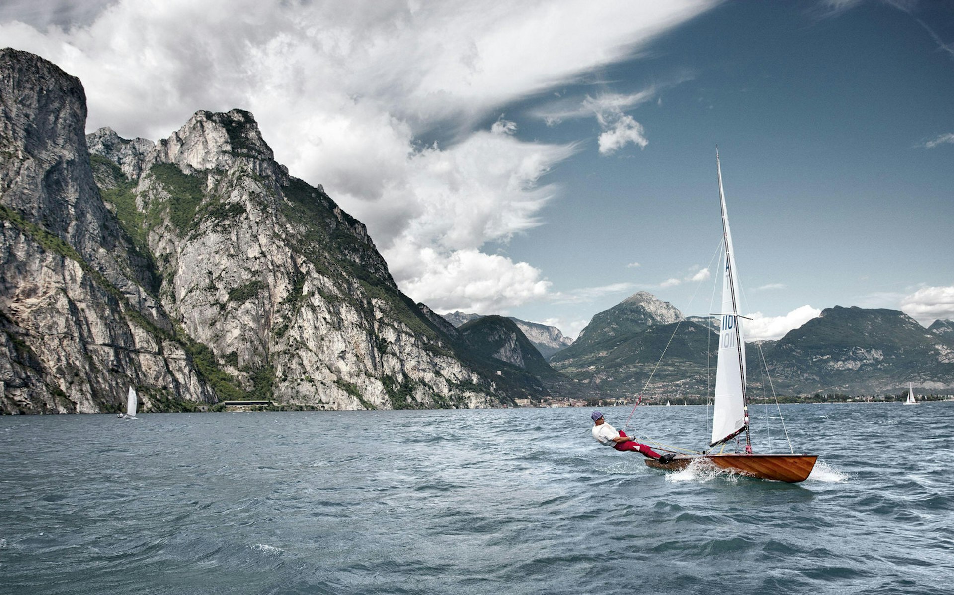 A sailor leans off the deck of his boat as he speeds through the waters of Lake Garda