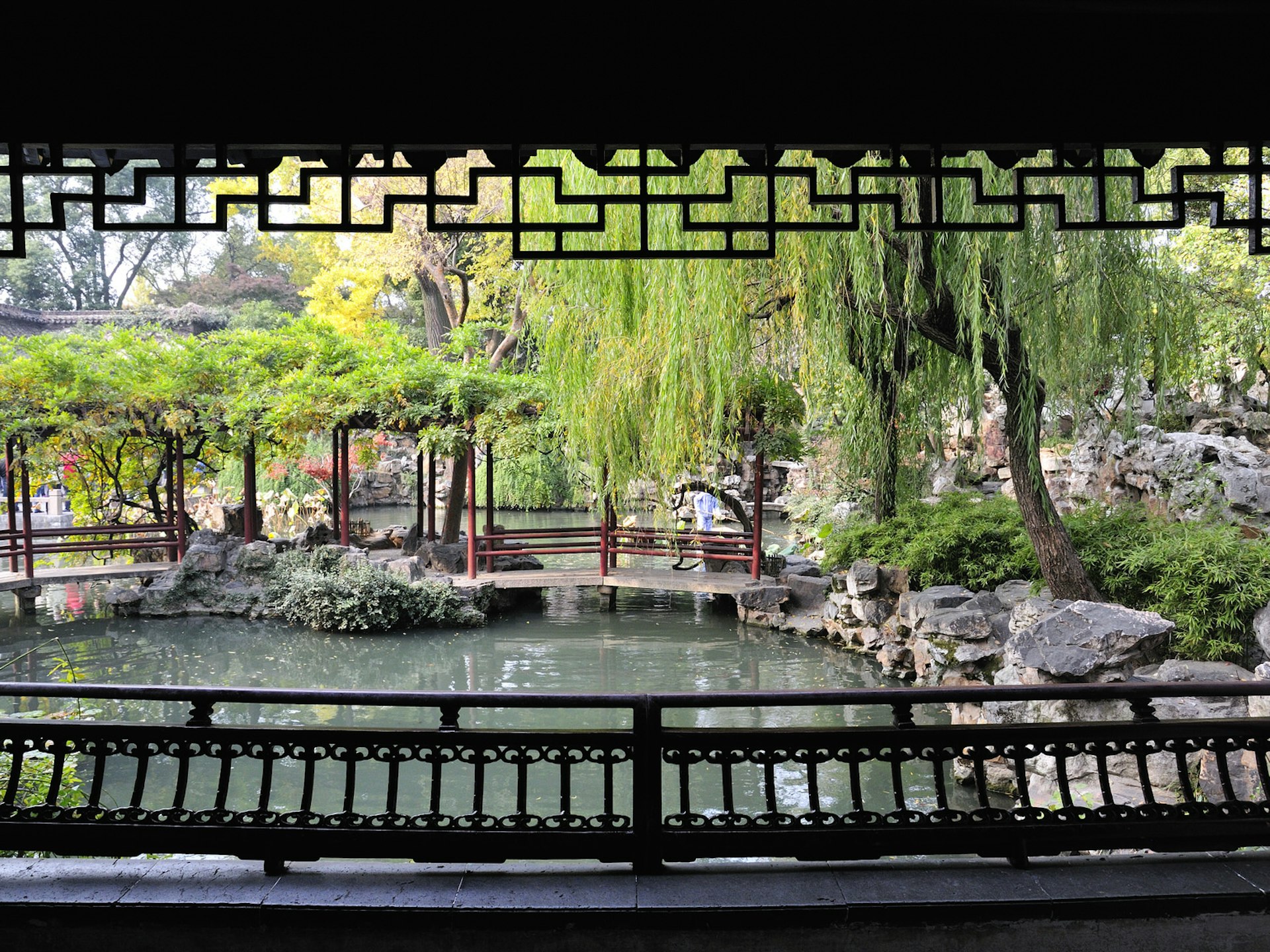 View from inside a covered pavilion, framed by wooden lattice, onto a pond with overhanging willow trees. Visiting a smaller garden at off-peak times is the best way to enjoy its intended tranquility © walkdragon / Shutterstock