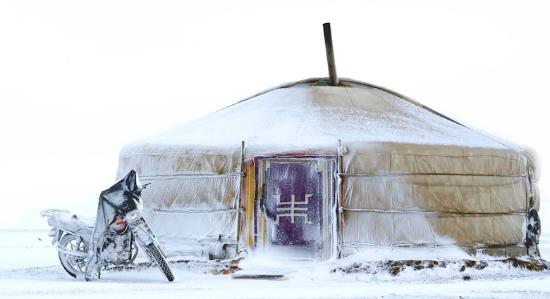 A yurt tent with a red door is covered in snow with a motorcycle iced over outside © Chantal de Bruijne / Shutterstock