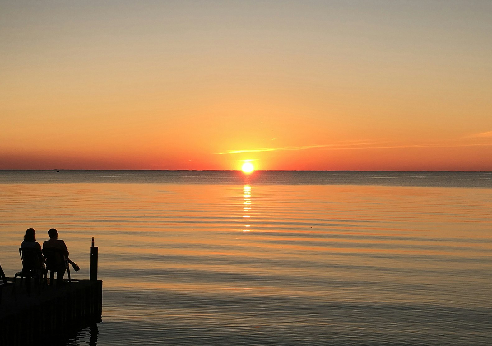 two people sit on a dock and watch a brilliant orange sunset on the coast of Door County