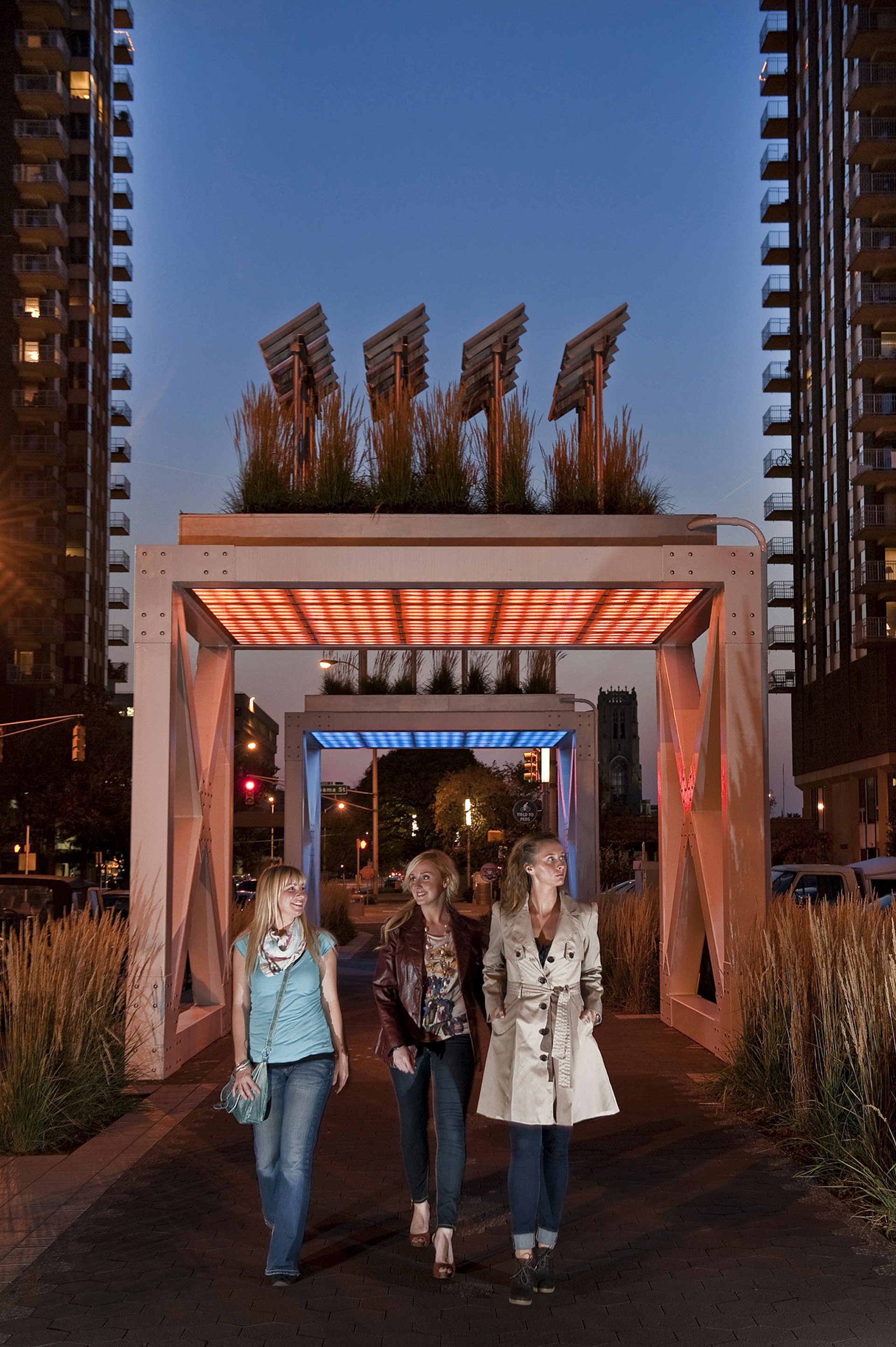 three women walk through a lighted public art gateway at night in Indianapolis