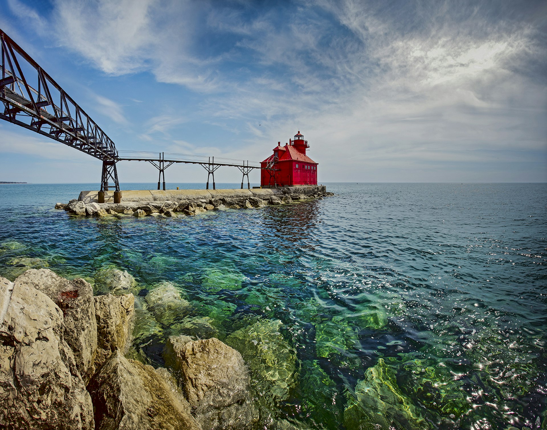 small red lighthouse sits in clear blue waters of lake michigan