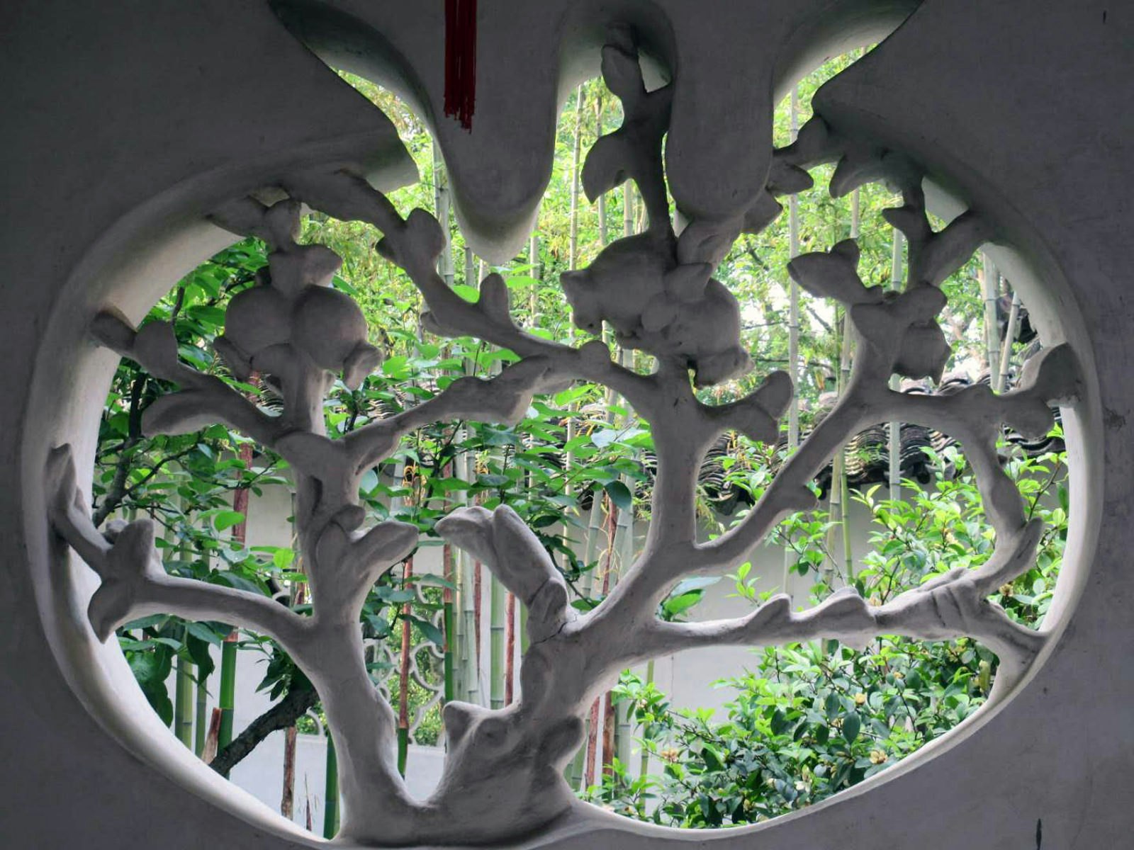 A white-washed window with delicate grating shaped like a tree looks out onto trees in the garden. Suzhou's classical gardens have details like this window that create picturesque scenes as you wander through © Tess Humphrys / Lonely Planet