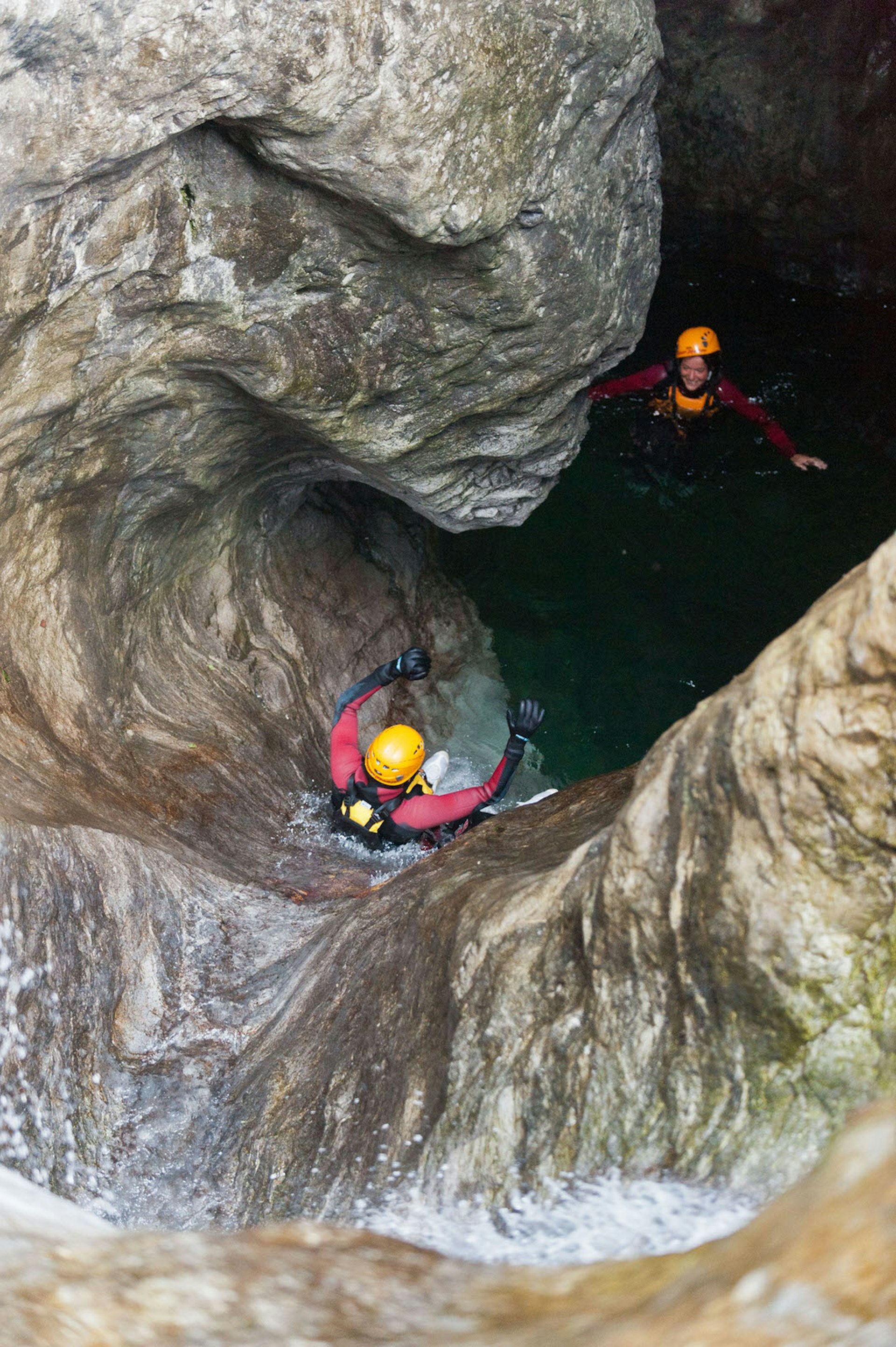 A helmeted canyoner slides down a rock chute into a deep pool