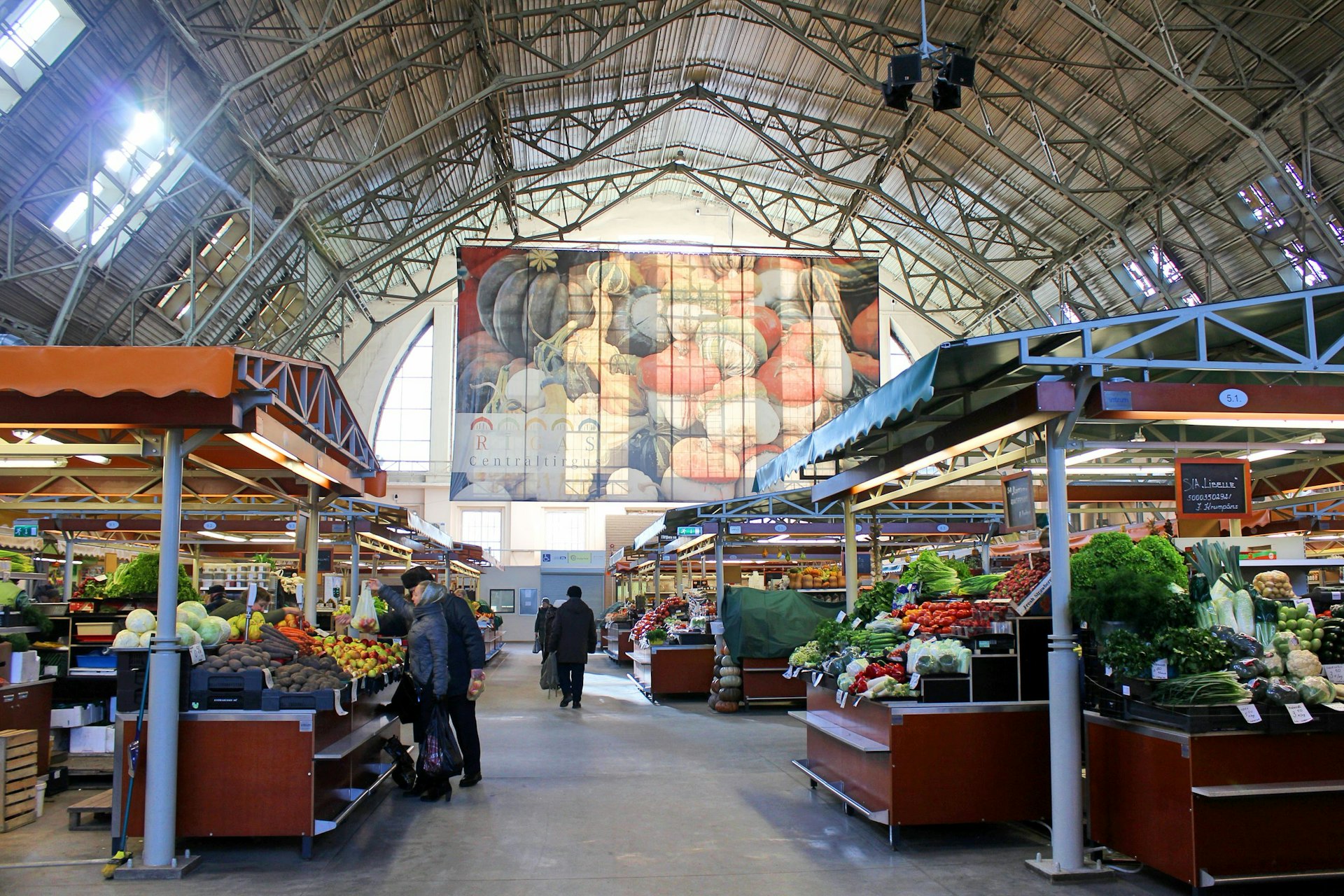 Customers browse the fresh produce on the stalls in one of the vast Zeppelin hangars that now make up Rīga Central Market © Caroline Hadamitzky / Lonely Planet