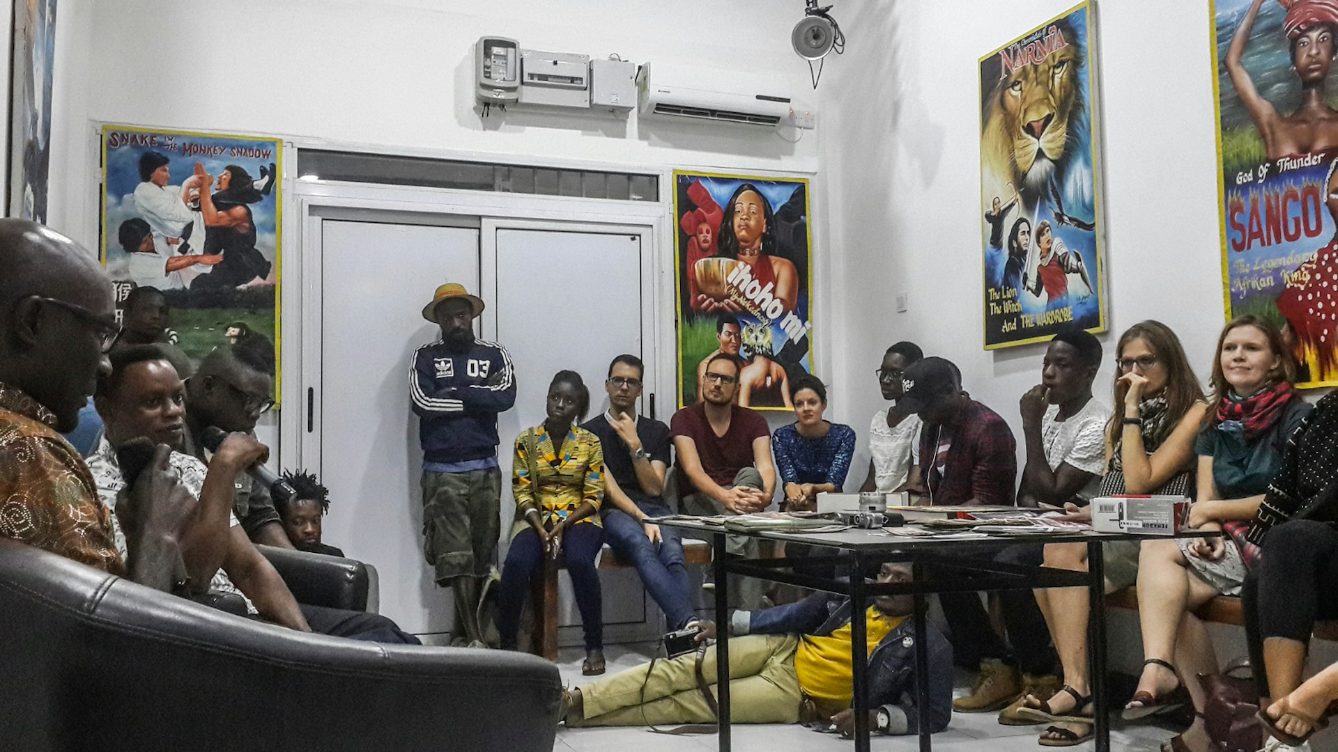 Within a small, stark white room people of African and European descent stand and sit along the walls, even lounging on the floor, while listening to a talk at The Studio © Elio Stamm / Lonely Planet