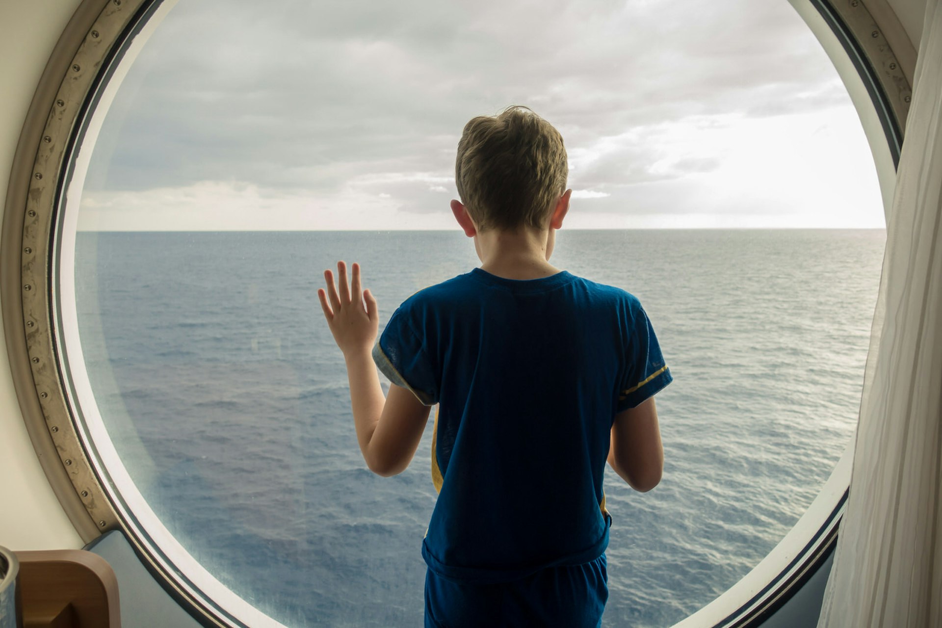 A young boy gazes out of a ship's porthole towards to sea © Fred Levy / EyeEm / Getty