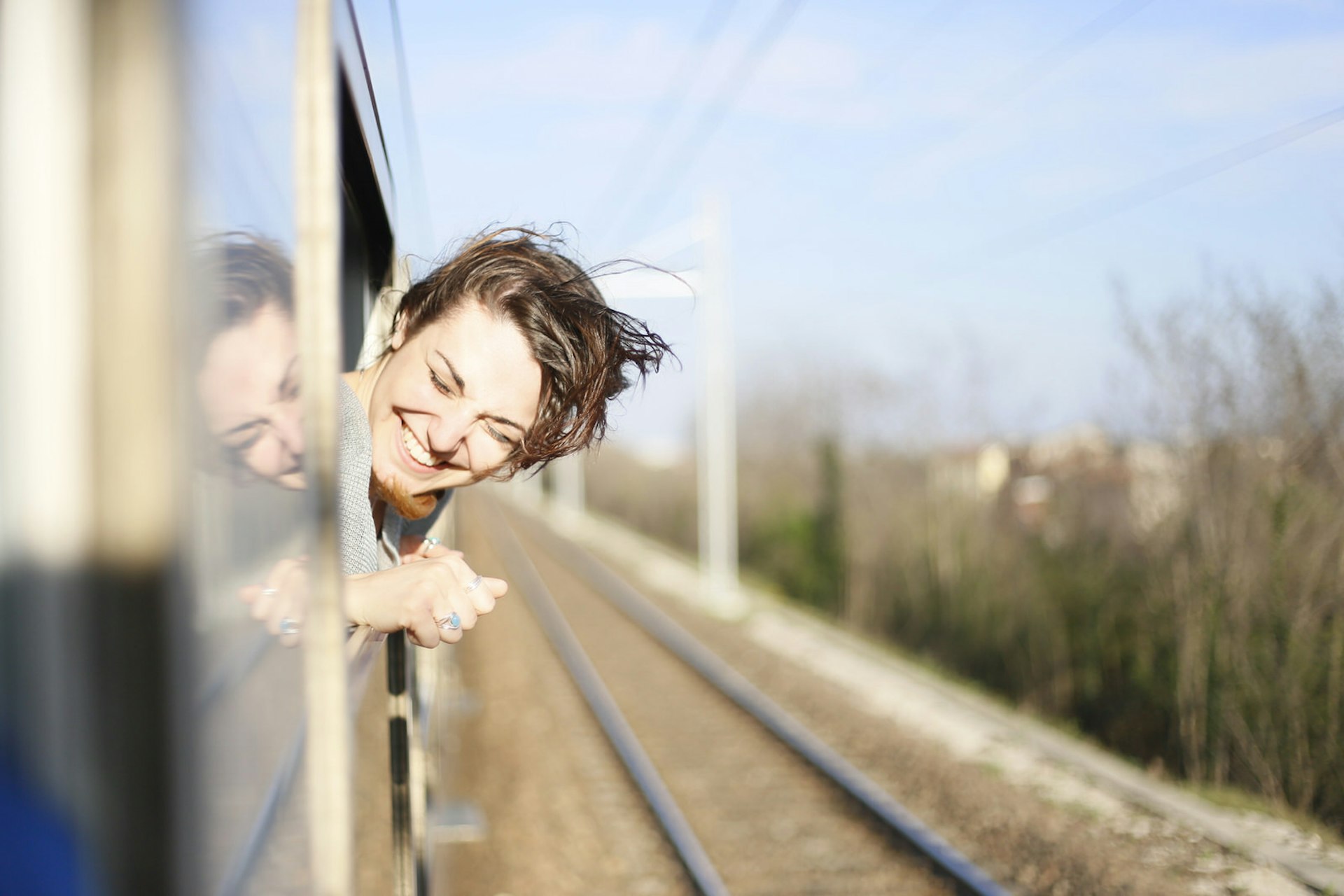 Young woman travelling on a train with her head out the window and the wind blowing her hair © Eleanor Joy Holmes / Getty Images 