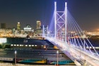 Stretching over eight rows of parked trains, the brilliantly lit white towers and cables of the Nelson Mandela Bridge stretch towards the skyline © Henrique NDR Martins / Getty Images