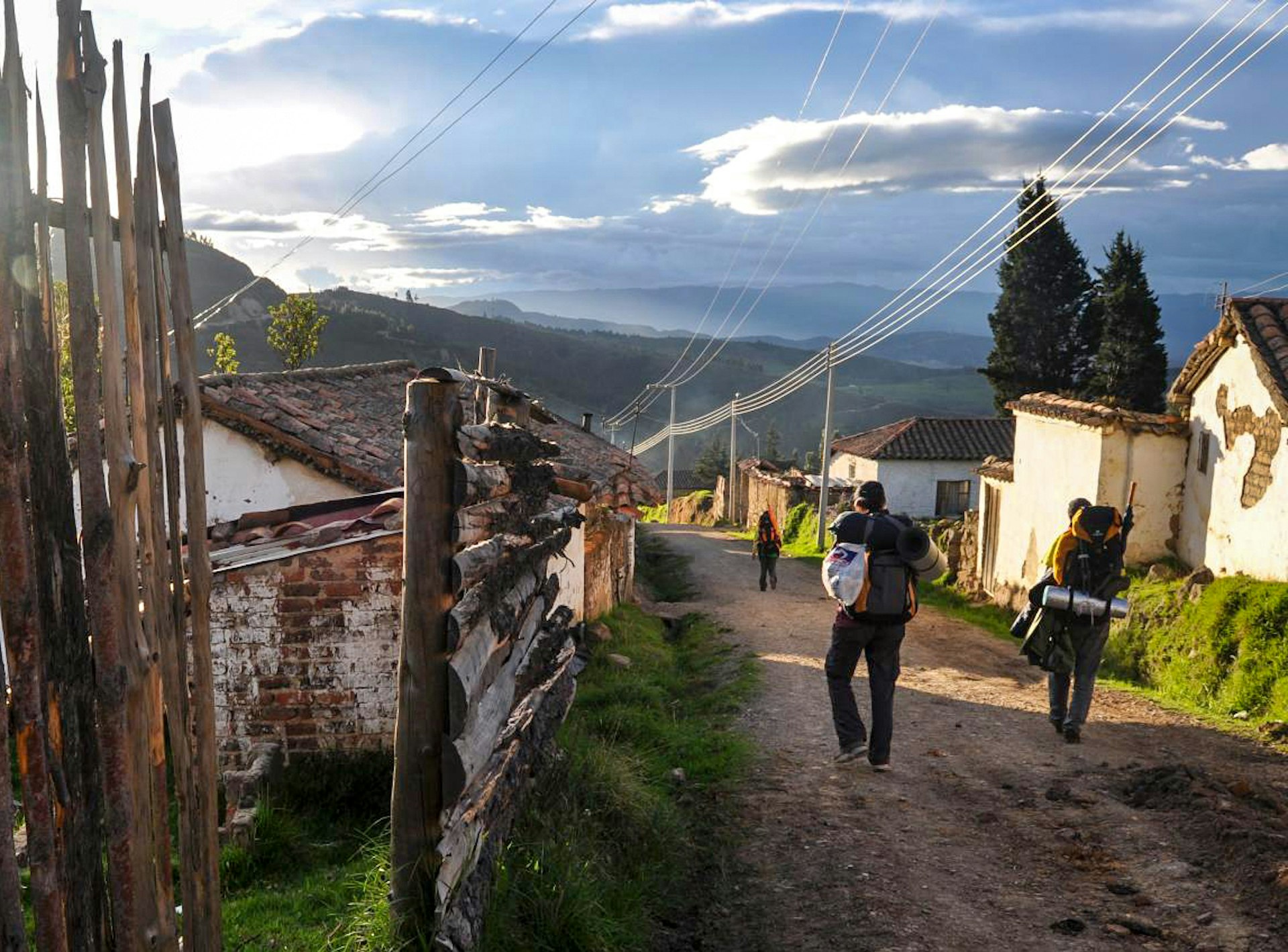 Travelers wearing backpacks walk on dirt road in Mongui