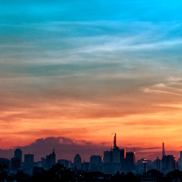 The jagged skyline of Nairobi's high-rises cuts a dark strip below a sky that moves from purple to a bright orage as moving upwards, finishing a bright teal colour ©Jude Gichumbi / 500px