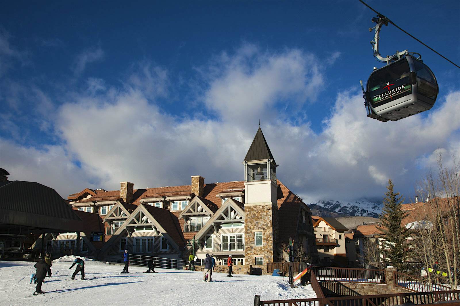 Features - USA, Colorado, Telluride, Mountain Village Ski Area gondola The Mountain Village Ski Area gondola passes overhead as people walk through the historic, snow covered town © Walter Bibikow / Getty Images