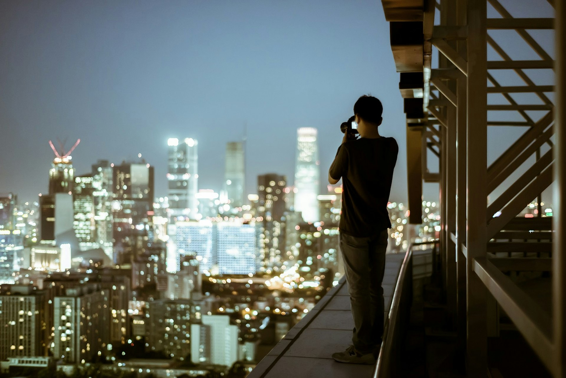 A man takes a photo of the dazzling Beijing skyline at night from a rooftop vantage point © DuKai photographer / Getty Images