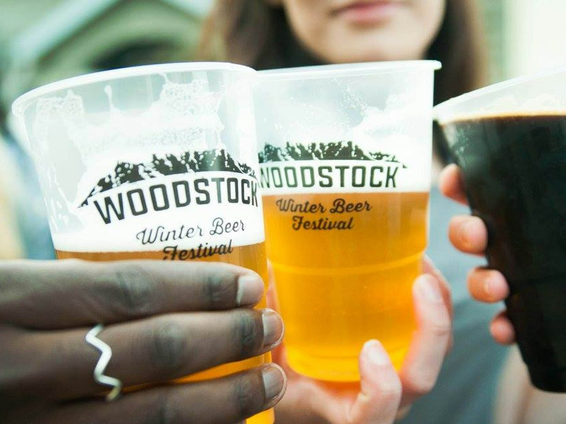 Alternative festivals - three people holding up plastic cups of beer with the Woodstock Winter Beer Festival logo on them