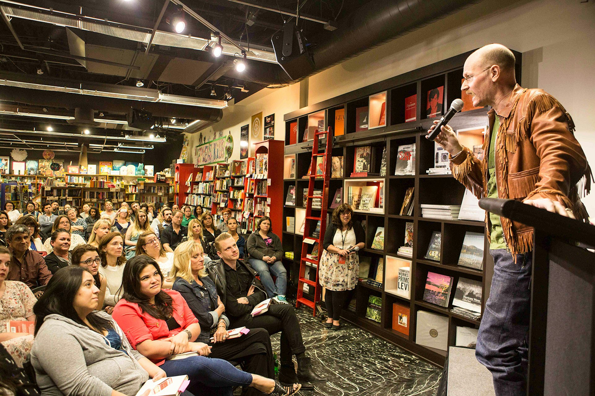 male author holding microphone speaks to audience in a bookshop