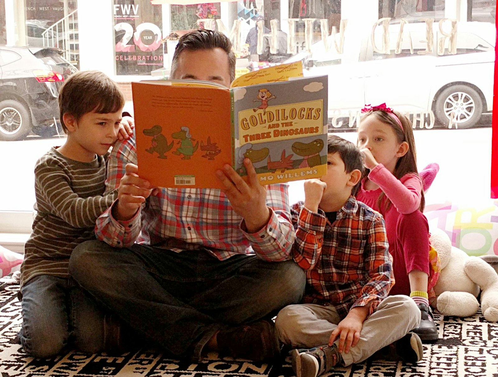 man reads to three children in a bookstore