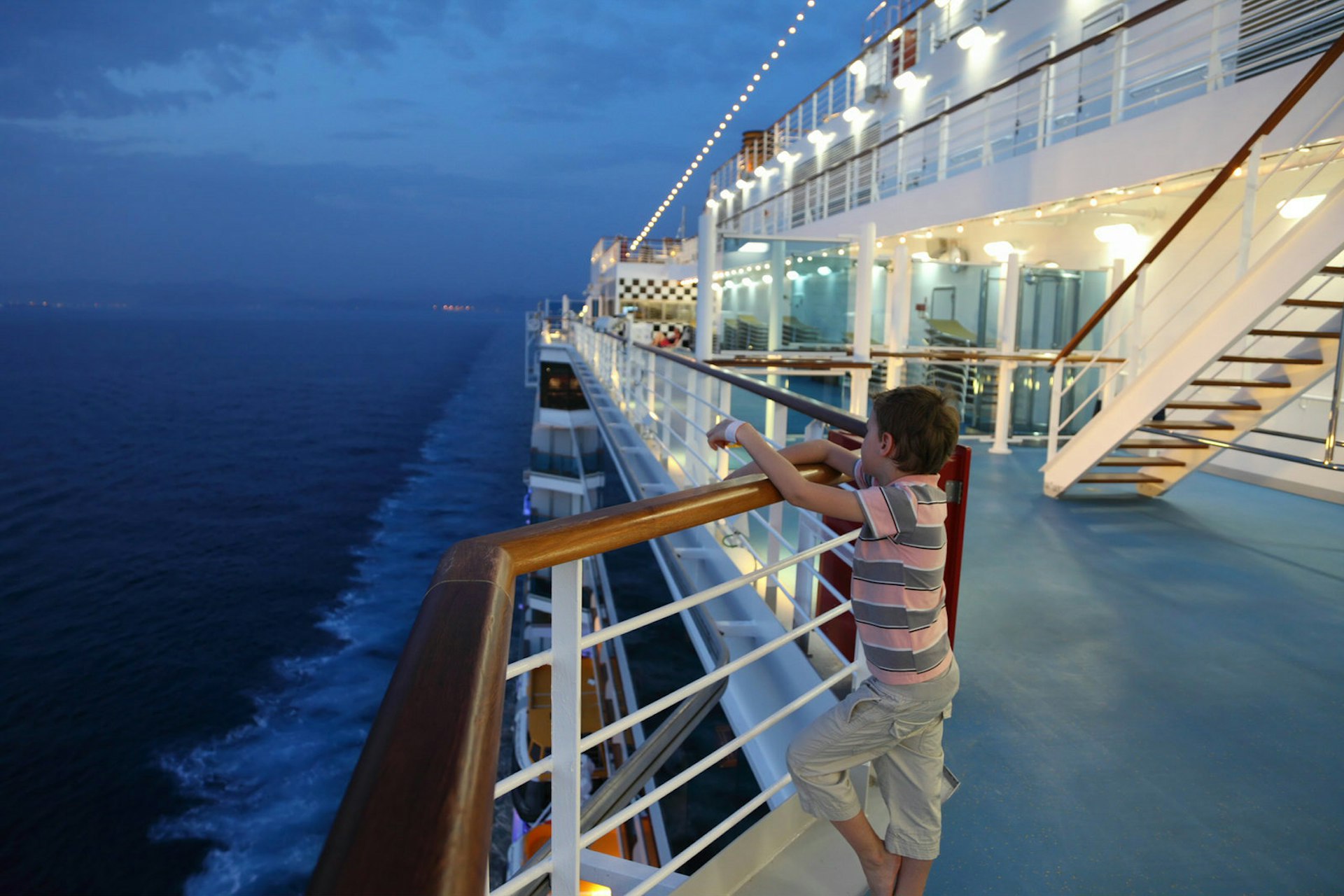 A young child looks over the balcony of a cruise ship as the sky grows dark © Pavel L Photo and Video / Shutterstock
