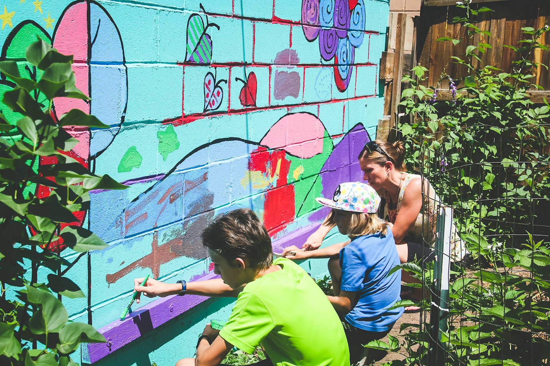 two children and an adult paint a green, blue and red mural of a dragon on the outer wall of a bookstore in Denver