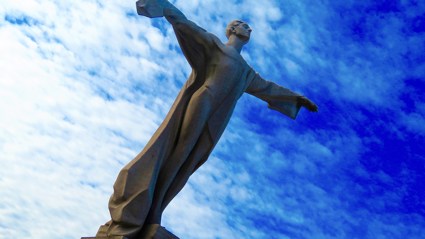 granite statue with outstretched arms against a blue sky in washington dc
