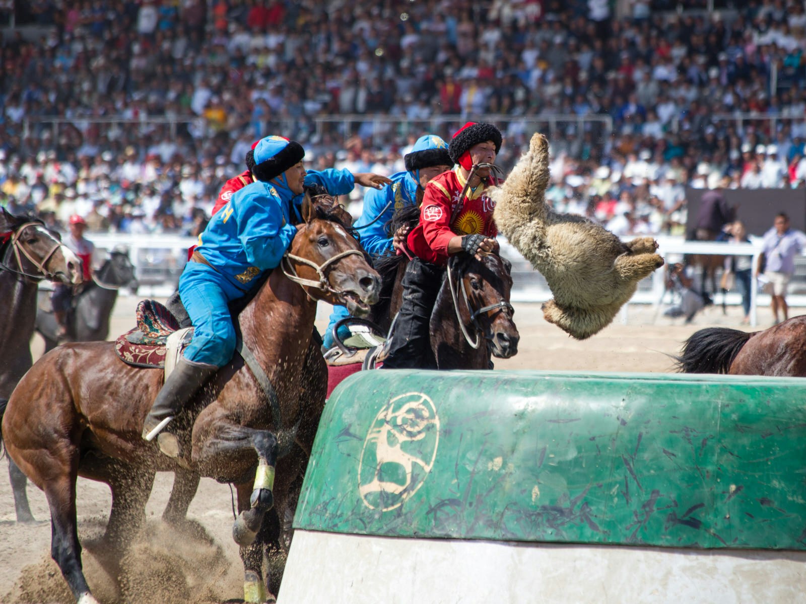 Horseback riders from two teams jostle with their horses for a goat carcass that flies through the air into the goal, in a packed stadium © Stephen Lioy / Lonely Planet