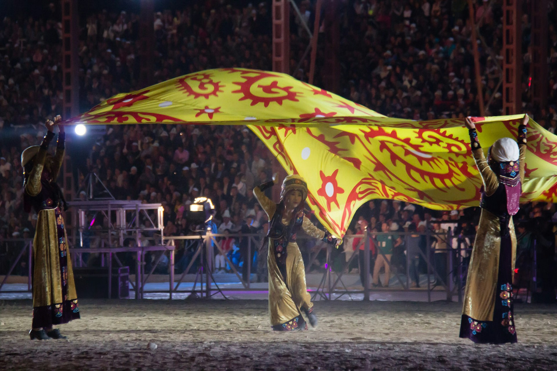Kyrgyz dancers twirl with a giant yellow flag inside a packed stadium for the 2014 World Nomad Games opening ceremony © Stephen Lioy / Lonely Planet