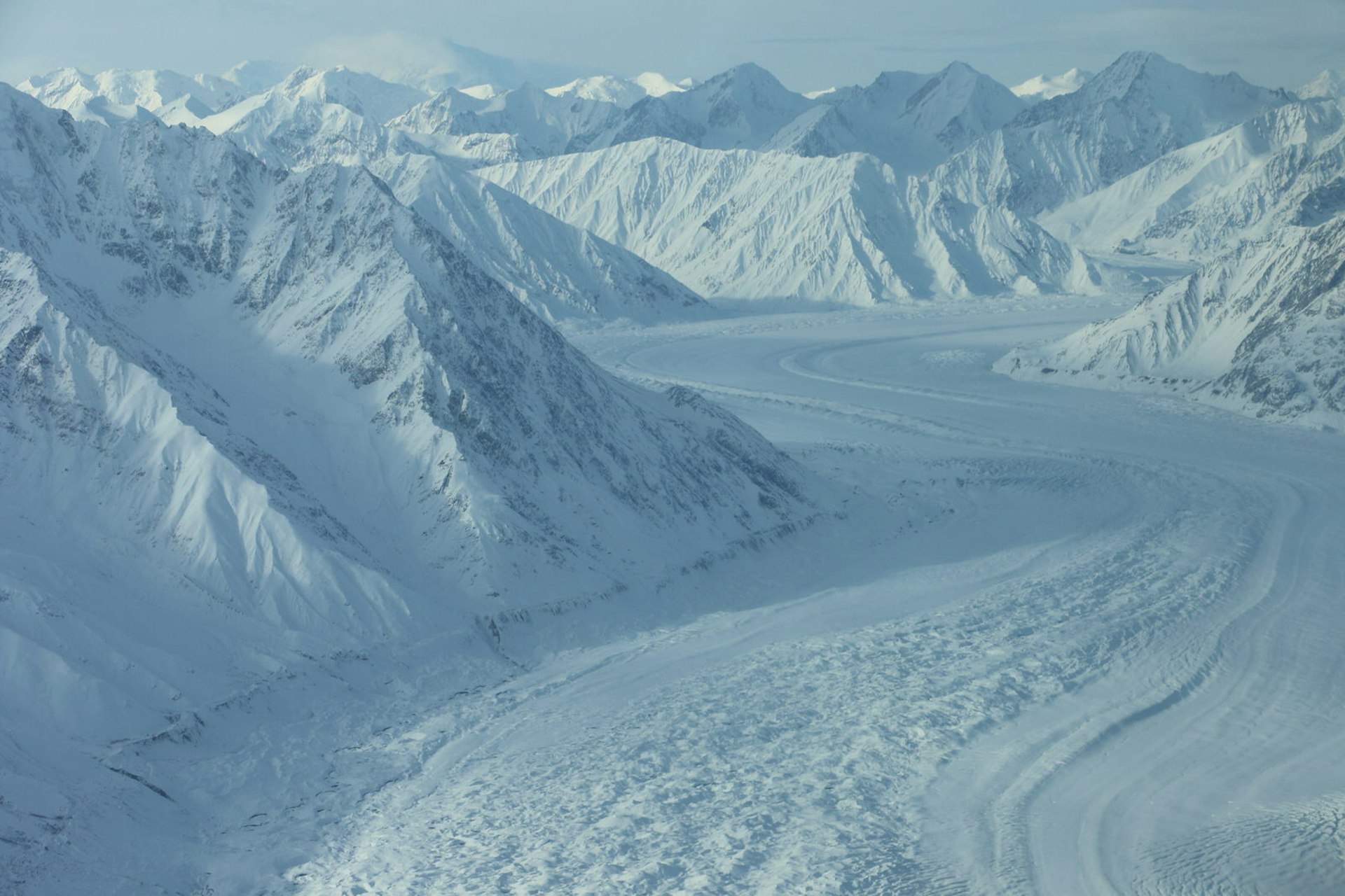 A river of ice fills the space between two sets of snow covered mountains, as seen from a small aircraft © Mike MacEacheran / Lonely Planet