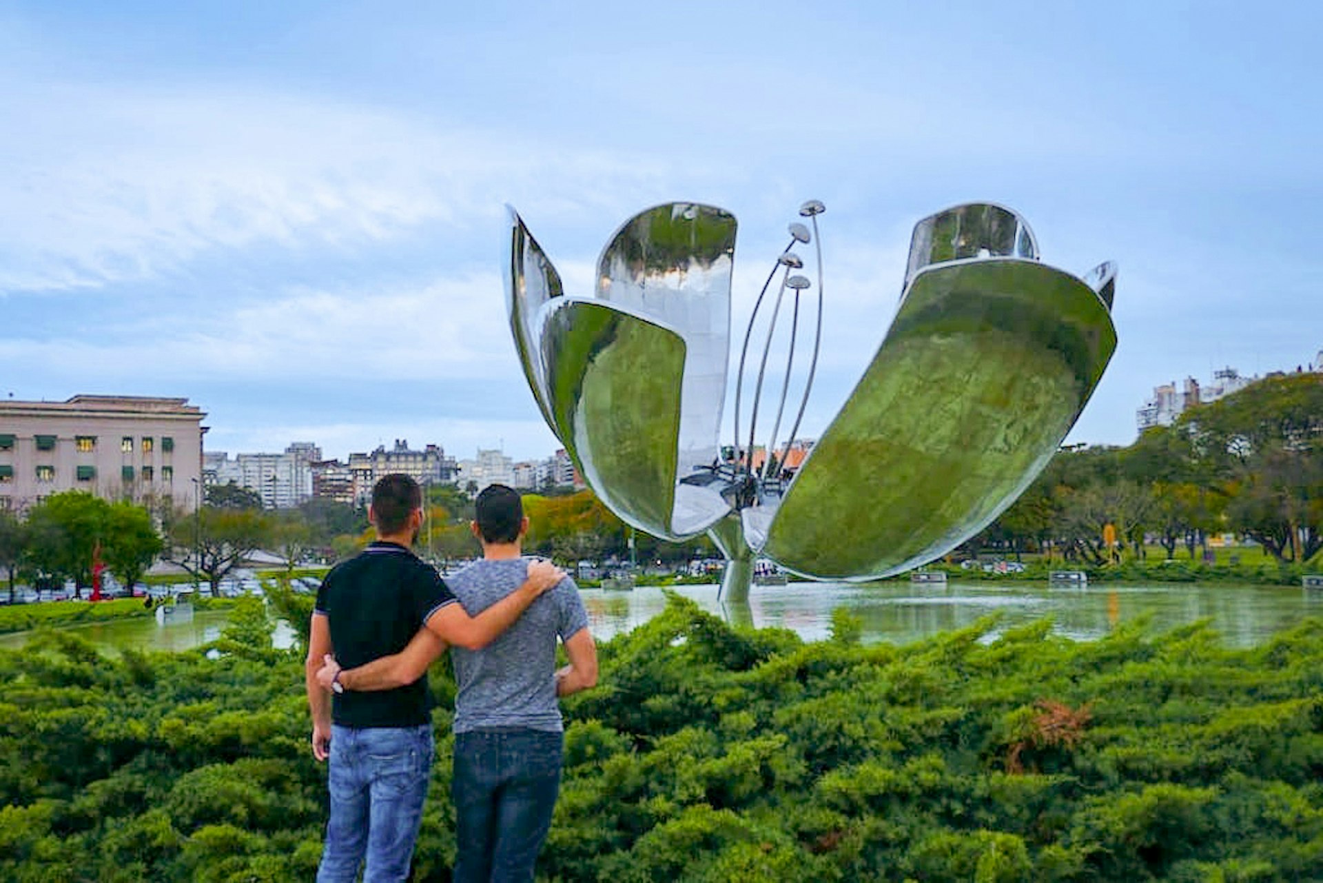 two men stand with arms around each other in front of large metal sculpture © Nomadic Boys / Lonely Planet