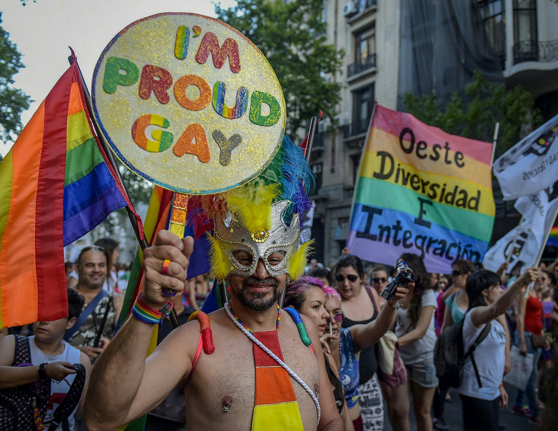 A shirtless man wears a masquerade mask and holds a sign that says "I'm Proud Gay"© JUAN MABROMATA / Getty Images