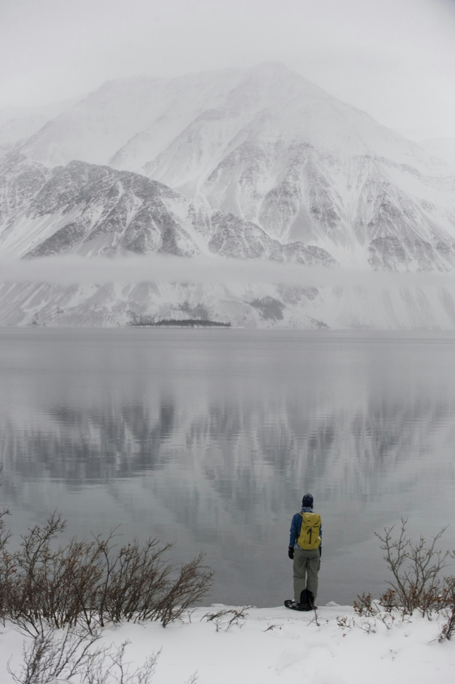 A woman snowshoeing in winter looks out over frozen Kathleen Lake, with a snow-covered mountain in the background reflected in the ice © Peter Mather / Getty Images