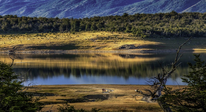 Two hikers face a lake with rolling green hills behind it