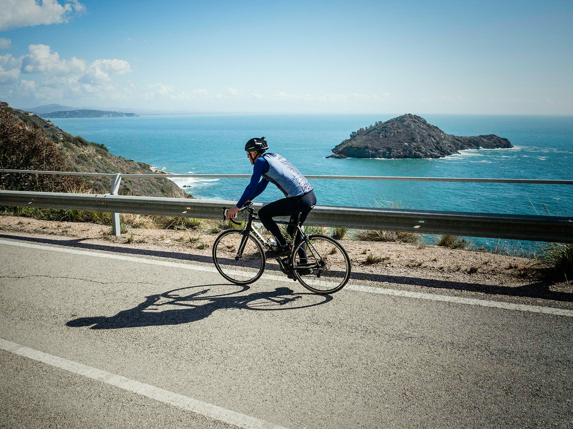 Writer Matt Phillips cycles down the road, which sits on the edge of a cliff - behind the barriers sits the Mediterranean and the forested islet of L'isolotto © Paolo Ciaberta