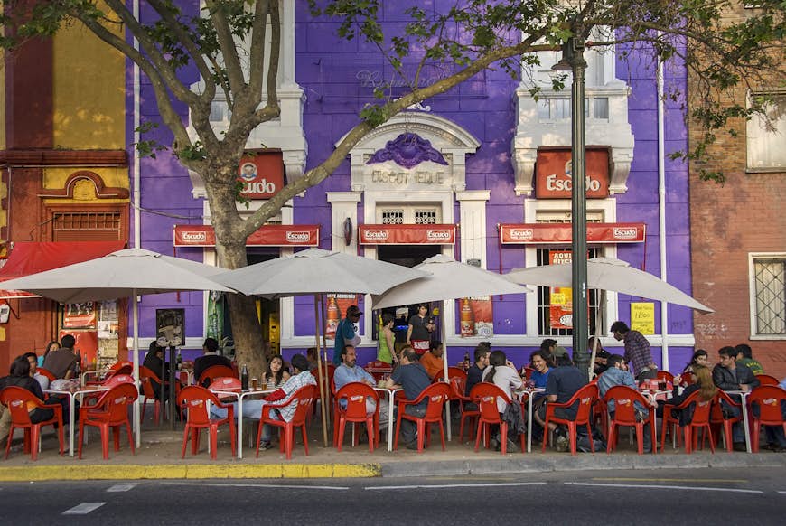 Patrons sit in red chairs at a sidewalk cafe in front of purple building© John Elk / Getty Images