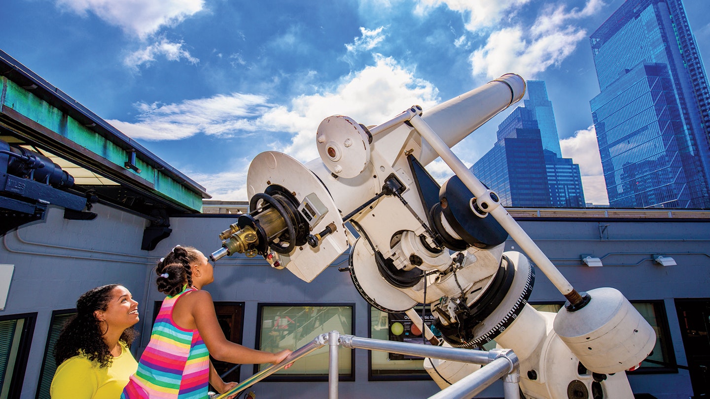 two children gaze into a telescope on a sunny day at the Franklin Museum J. Fusco for VISIT PHILADELPHIA®
