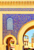 The golden arches of Fez's Blue Gate Bab Boujelud reveal life inside the medina; between the arches and gold trim, the large gate is decorated in delicate blue floral tiles.
