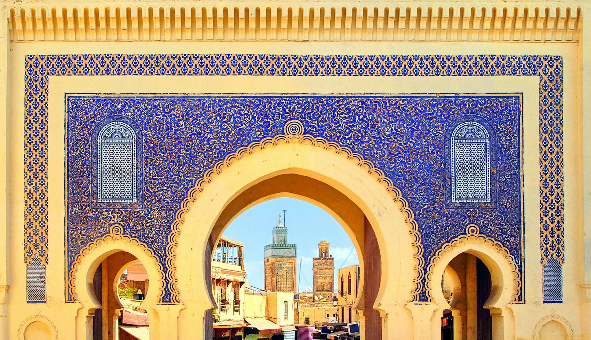 The golden arches of Fez's Blue Gate Bab Boujelud reveal life inside the medina; between the arches and gold trim, the large gate is decorated in delicate blue floral tiles. 