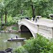 Two people row a small boat beneath Bow Bridge in Central Park in summer, as others cross the bridge on foot. © Amanda Hall / robertharding / Getty Images