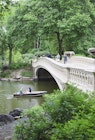 Two people row a small boat beneath Bow Bridge in Central Park in summer, as others cross the bridge on foot. © Amanda Hall / robertharding / Getty Images