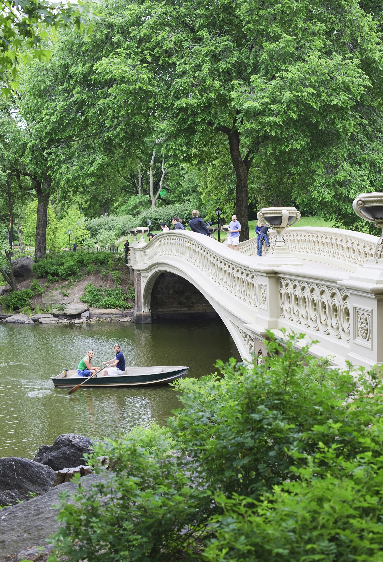 Two people row a small boat beneath Bow Bridge in Central Park in summer, as others cross the bridge on foot © Amanda Hall / robertharding / Getty Images