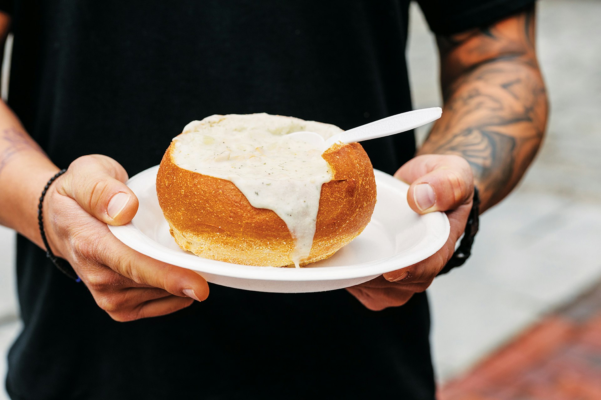 man with tattoos holds plate with bread bowl brimming with clam chowder © Adam DeTour / Lonely Planet