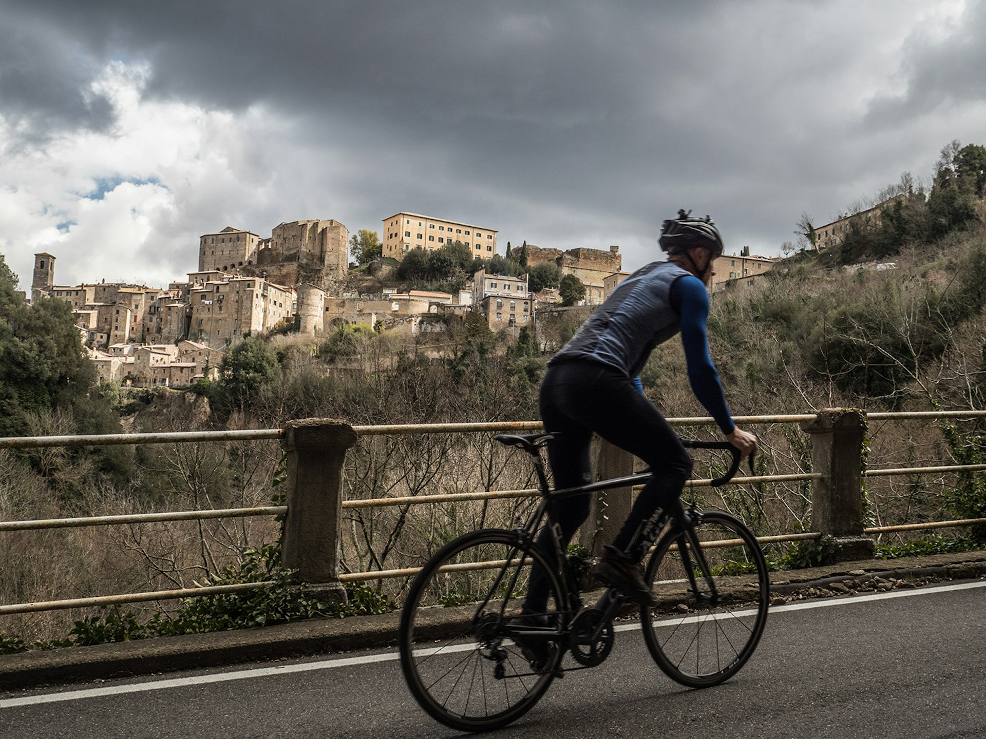 A cyclist stands out of the saddle and pedals up a hill with the village of Pitigliano in the background © Paolo Ciaberta