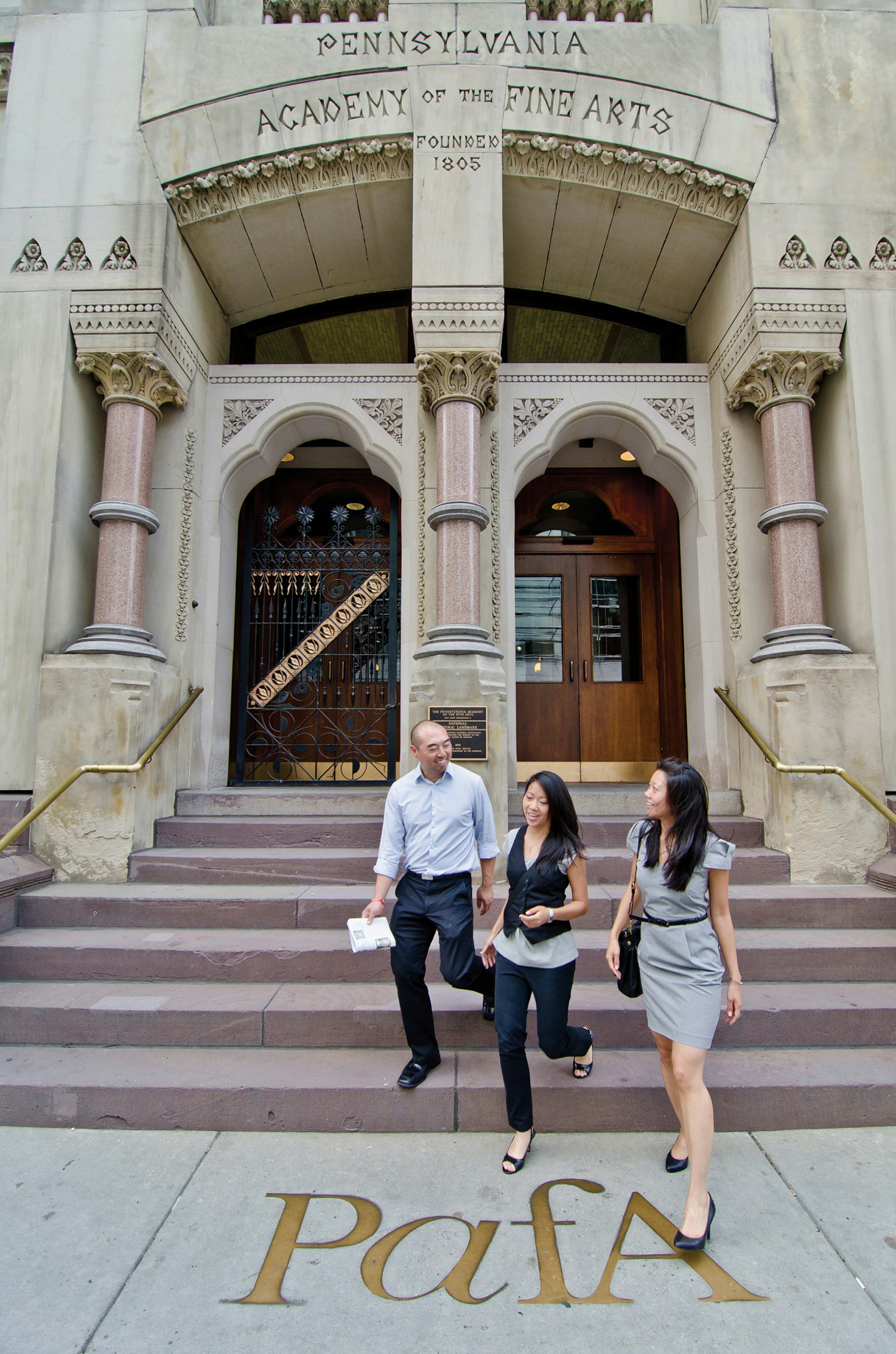two women and a man walk down the front steps of the Pennsylvania Academy of Fine Arts in Philadelphia