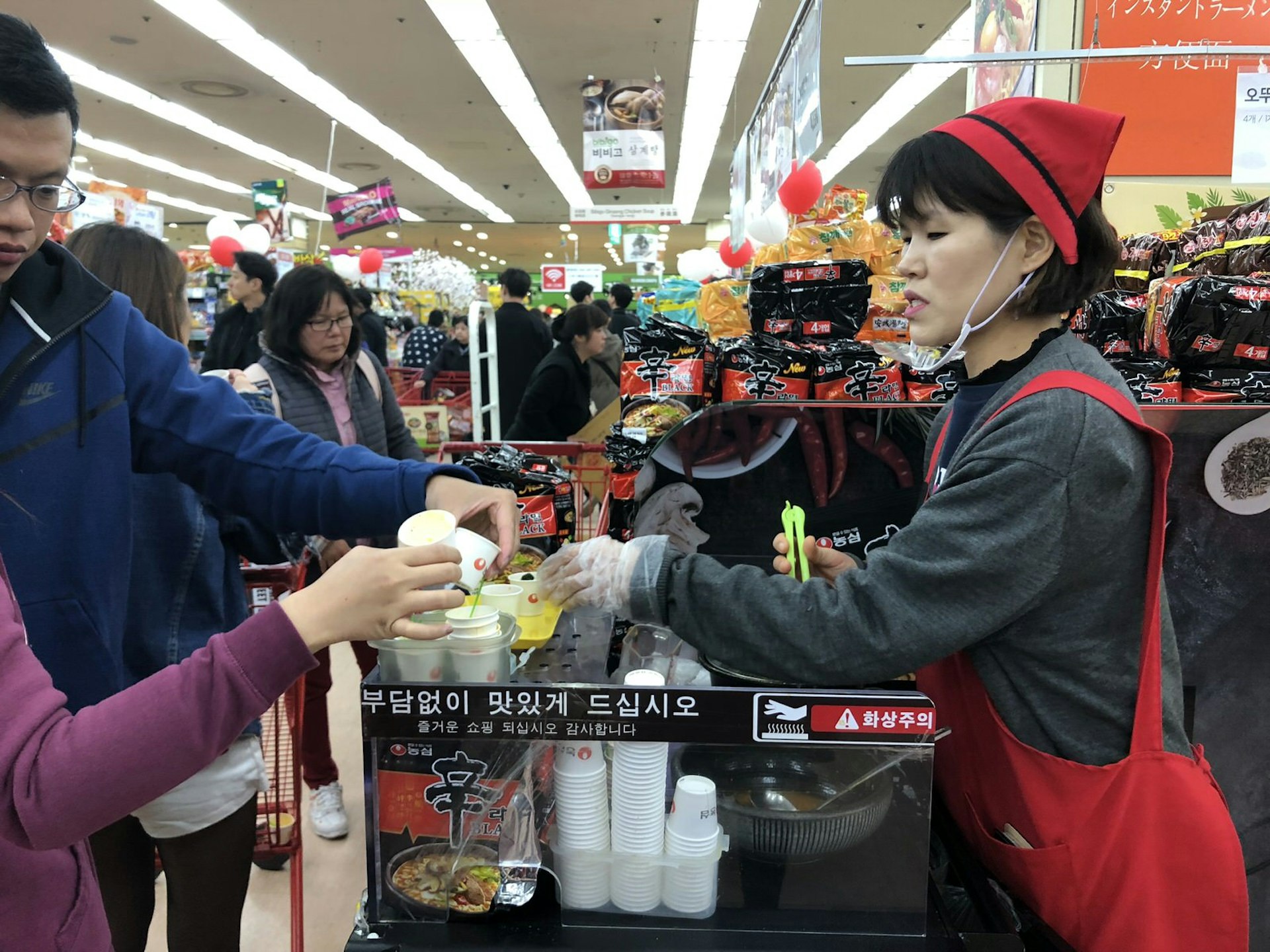 A sample-giver clad in a red apron and hat offer samples in paper cups. Free dinner? Opt for samples at the Lotte Mart in Seoul Station © Hahna Yoon / Lonely Planet