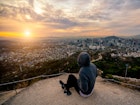 A hiker in a hoodie watches a pink and orange sunrise sitting on a rock overlooking Seoul city. Freeview: vistas of Seoul can be had via a free and gentle hike up Inwangsan © Mongkol_Chuewong / Shutterstock