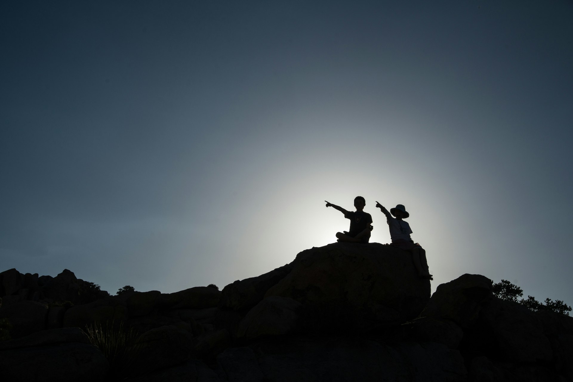 Two children in silhouette sitting on a rock in Joshua Tree National Park in California