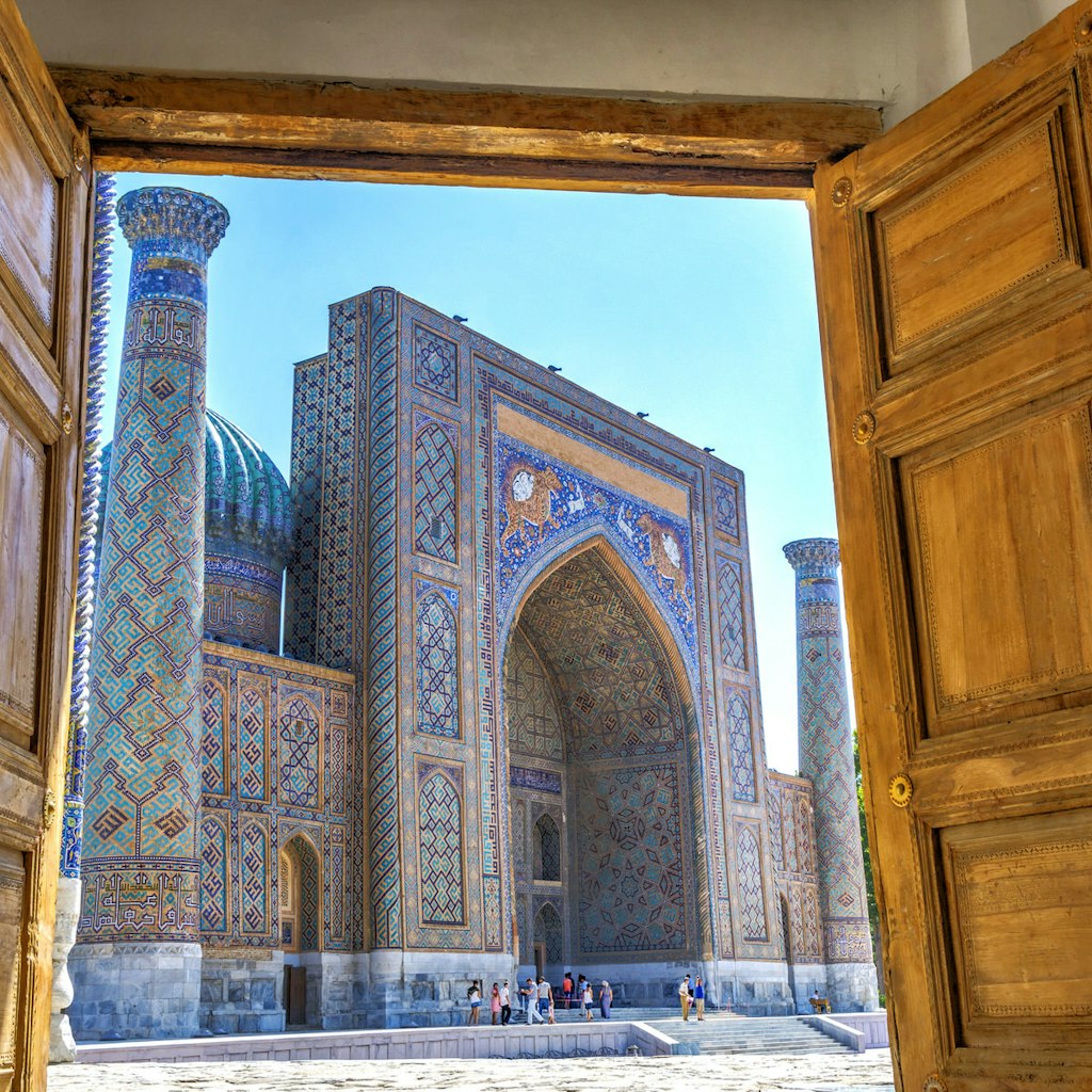 Wooden doors open onto a sunny blue-tiled Islamic square. Uzbekistan's new policies are making it easier to visit its stunning monuments, such as the Registan © Dinozzzaver / Shutterstock